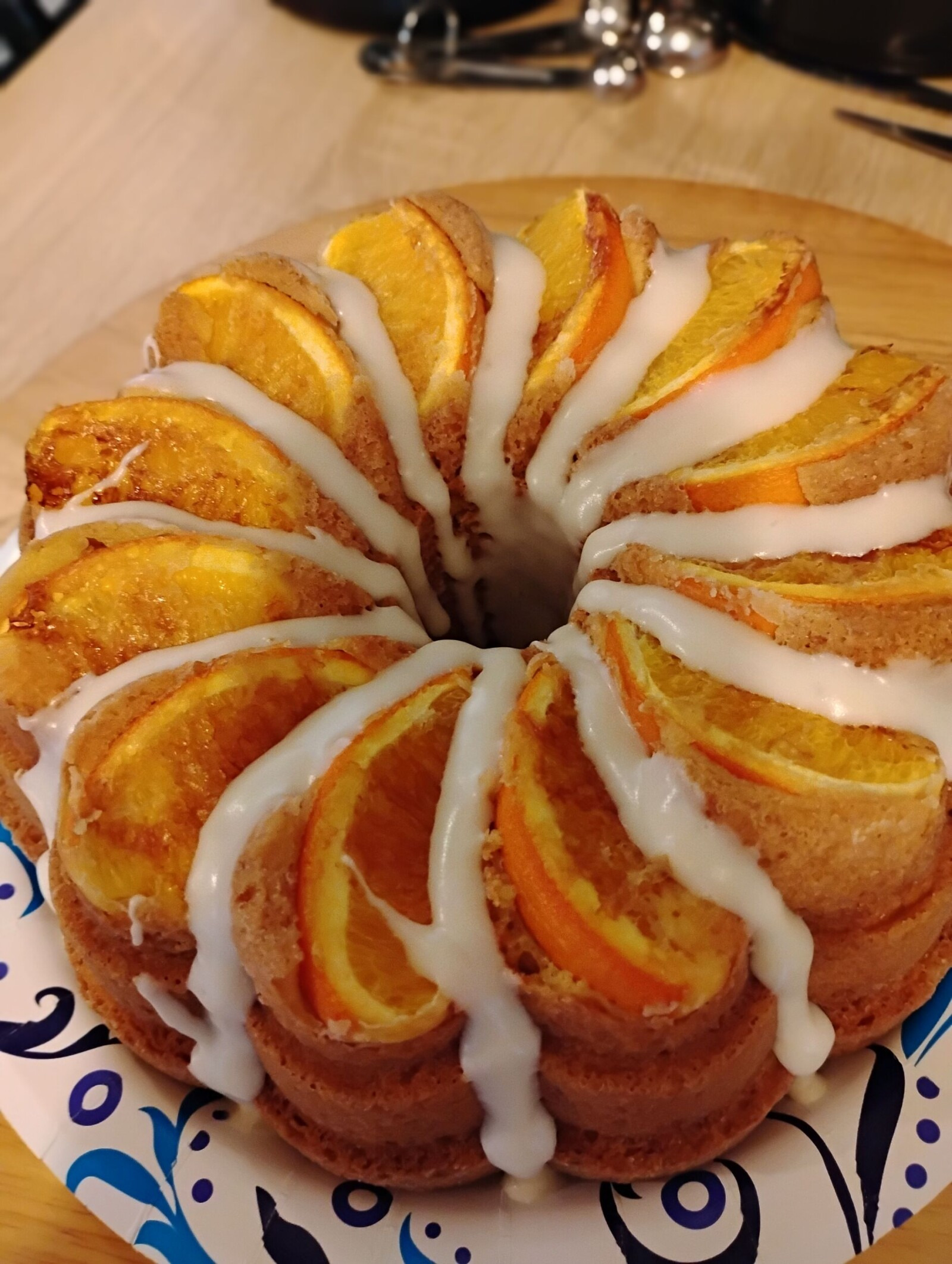 Citrus bundt cake topped with orange slices and white icing, on a blue patterned plate.