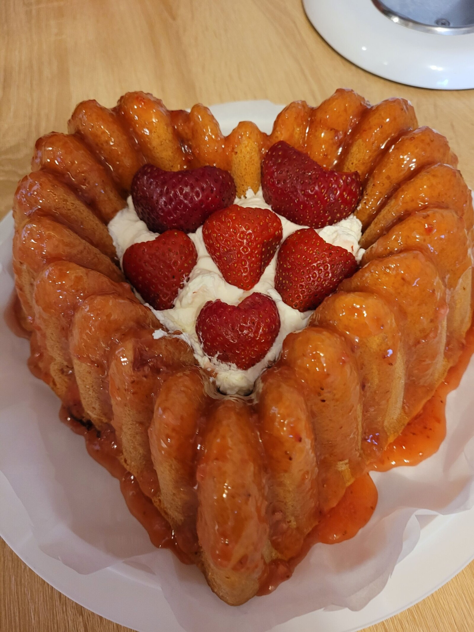 Heart-shaped strawberry upside-down bundt cake with glaze, cream, and fresh strawberries on a white plate.